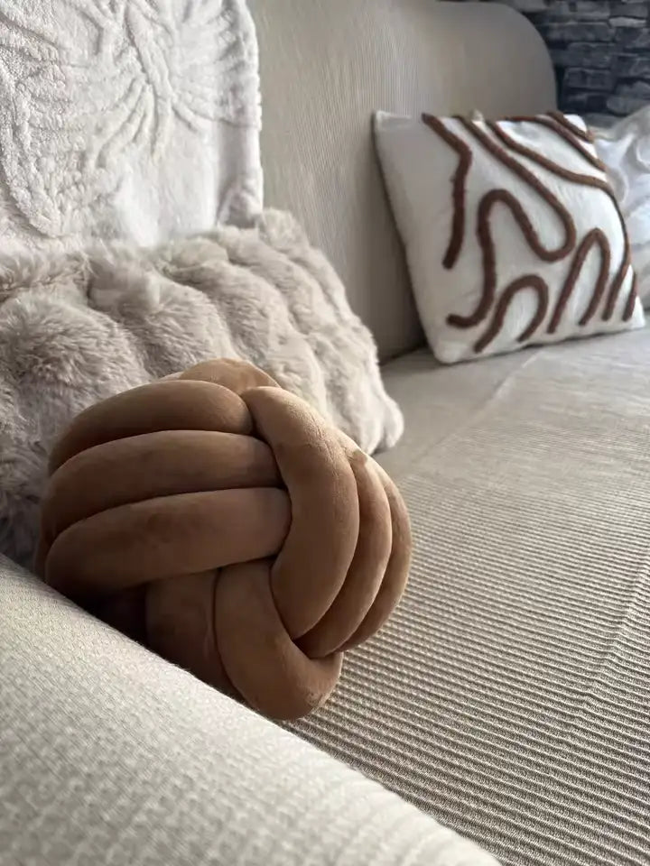 Un coussin de jet noué, bronzé et moelleux reposant sur un canapé beige.
