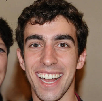 Un homme souriant aux cheveux noirs, bouclés et au teint clair.